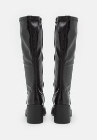 Bottes noires en cuir jusqu'aux genoux avec une texture lisse, dotées d'un talon épais et de fermetures éclair latérales. Des coutures distinctives sont visibles.