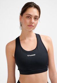 Svart sportbh med rundad halsringning, elastisk band och vitt logo. Tillverkad i mjukt, stretchigt material för komfort och passform.