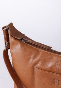 Brown leather handbag with a smooth texture, angled design, zip closure, and silver hardware. Features a front pocket with stitching detail.