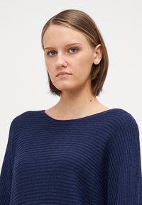 Navyblauwe gebreide trui met een geribbelde textuur, brede halslijn en een ontspannen pasvorm. Geen zichtbare hardware of extra patronen.