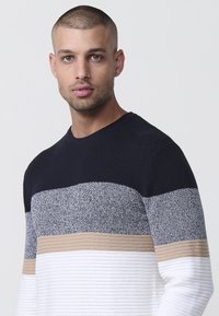 Suéter de punto con rayas horizontales en azul marino, gris, beige y blanco. Presenta un escote redondo y detalles de tejido texturizados.