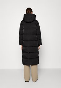 Langer schwarzer Puffer-Mantel mit Kapuze, mit horizontalen gesteppte Abschnitten, glatter Oberfläche und knielangem Design. Keine sichtbare Hardware.