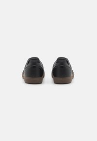 Black leather slip-on shoes with textured sides, a brown rubber sole, and subtle stitching detail at the heel and back for support.