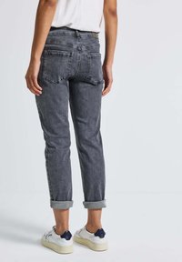 Jean en denim gris à jambe fuselée et avec des ourlets retroussés. Comprend deux poches arrière et une texture de lavage subtile. Associé à des baskets blanches.