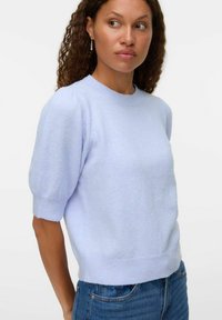 Pull en tricot bleu clair avec des manches courtes bouffantes et un col rond. Texture douce, poignets et ourlet côtelés. Porté avec un jean en denim bleu.