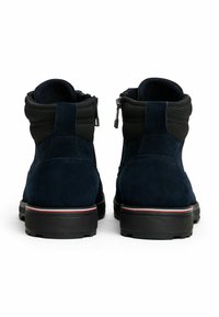 Une paire de bottines en suede bleu foncé avec des cols rembourrés noirs, des fermetures éclair à l'arrière et des semelles épaisses noires avec des accents rouge et blanc.