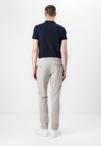 Marineblå stripete polo-shirt kombinert med lysegrå bukser og hvite joggesko. Bakfra viser den slim-fit skreddersydde detaljer og justerbare midjedetaljer.