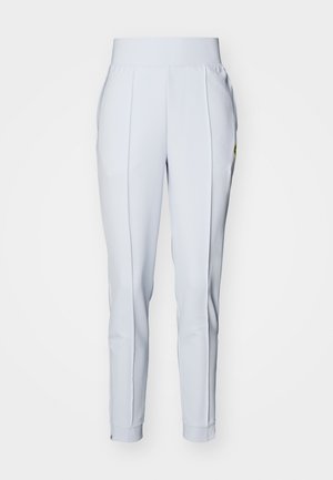 Lys grå treningbukser med bred elastisk midjebånd, smale ben, subtile folder og glidelåsdetaljer ved anklene.