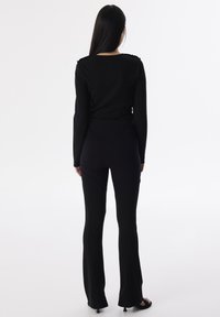 Schwarzes Langarmshirt mit rundem Ausschnitt und gerafften Schulterdetails, kombiniert mit schwarzen, weit geschnittenen Hosen mit Nahtakzenten.