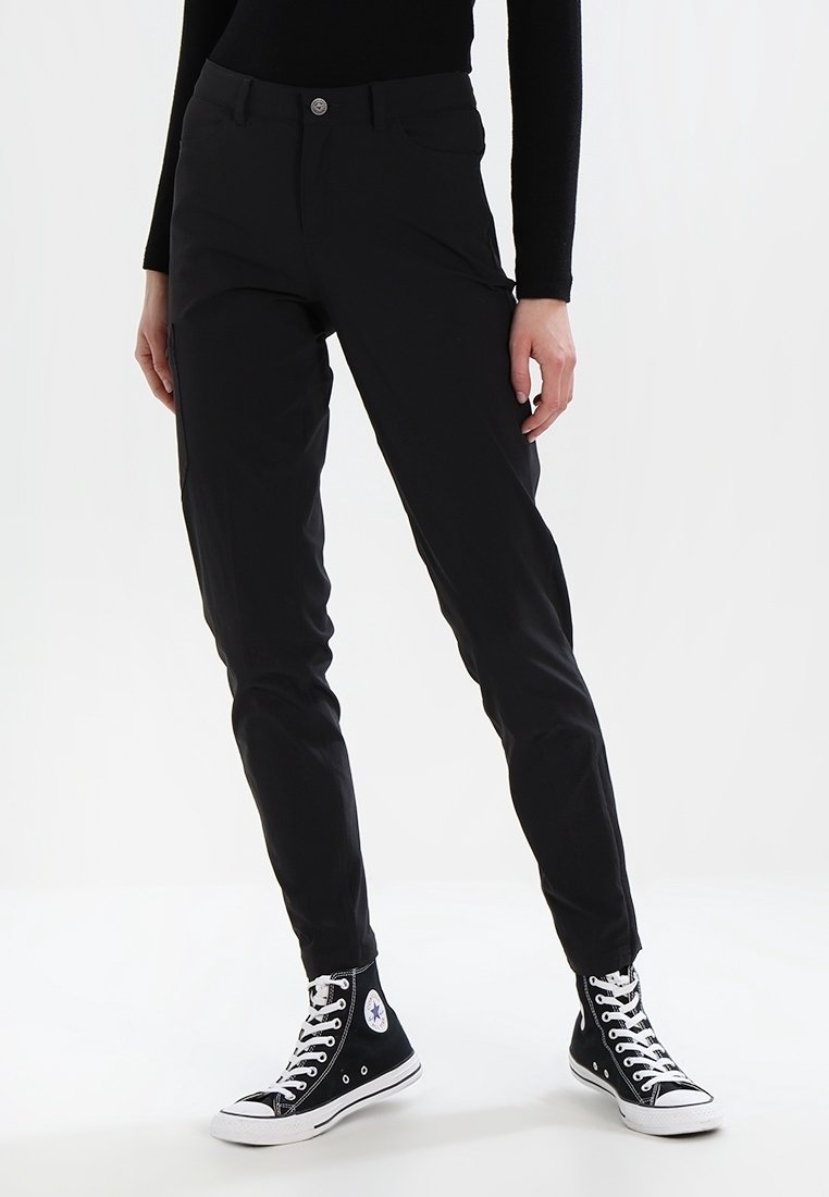 Černé slim-fit kalhoty s hladkou texturou, vybavené zapínáním na knoflík a kapsami. Nošeny s černými teniskami s vysokým svrškem.