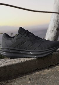 Baskets de sport noires avec dessus texturé et semelle rembourrée reposant sur un rebord en pierre à l'extérieur au crépuscule.