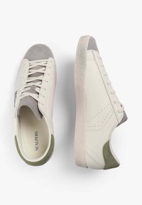 Zapatillas blancas de cuero con detalles en ante gris, suelas beige texturizadas y perforaciones decorativas. Logo en el lado. Diseño elegante y moderno.