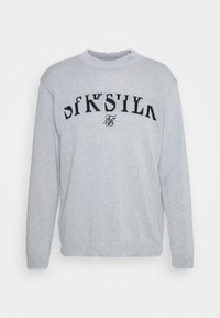 Sweater en tricot gris avec un col rond, présentant un design graphique en texte noir sur la poitrine. Texture douce et coupe décontractée.