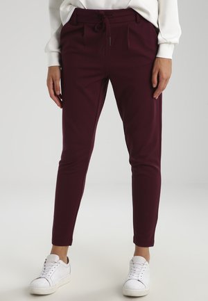 Burgunderfarbene, taillierte Hose mit einem Kordelzugbund, vorderen Falten, Seitentaschen und einem glatten Stoff, kombiniert mit weißen Sneakers.