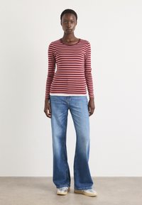 Maglietta a maniche lunghe bordeaux e rosa a righe con scollatura tonda, abbinata a jeans in denim a gamba larga di colore azzurro chiaro e sneakers beige.