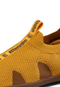 Gelbe gestrickte Schuhe mit braunen Akzenten, flexibles Design, Slip-On-Konstruktion und gebrandeter Zuglasche an der Ferse. Texturierte Oberfläche.
