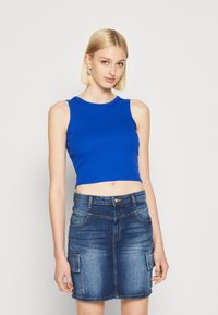 Top corto de canalé azul con cuello redondo, combinado con una falda ceñida de mezclilla oscura que cuenta con bolsillos laterales y un ligero desvanecimiento.