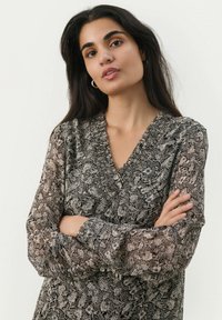 Langdoorstrik blouse in zwart met ingewikkelde witte bloemenpatronen, met een V-hals en geplooide details langs de halslijn.