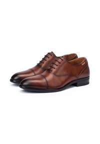 Scarpe eleganti in pelle marrone con una texture liscia, punta arrotondata e dettagli di cucitura sottili. Caratterizzate da cinque passanti con lacci neri e un tacco basso.