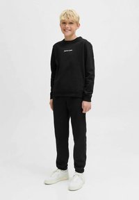 Μαύρο βαμβακερό φούτερ με στρογγυλή λαιμόκοψη, διακοσμημένο με λευκή λογότυπη επιγραφή. Συνδυάζεται με μαύρη φόρμα και λευκά αθλητικά παπούτσια. Σετ άνετης καθημερινής ένδυσης.