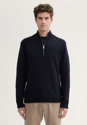 Marineblaue Strickjacke mit Reißverschluss und geripptem Kragen sowie Bündchen, ausgestattet mit einem Frontreißverschluss bis zur Mitte und strukturierten Schulterdetails. Weiche Stoffoberfläche.