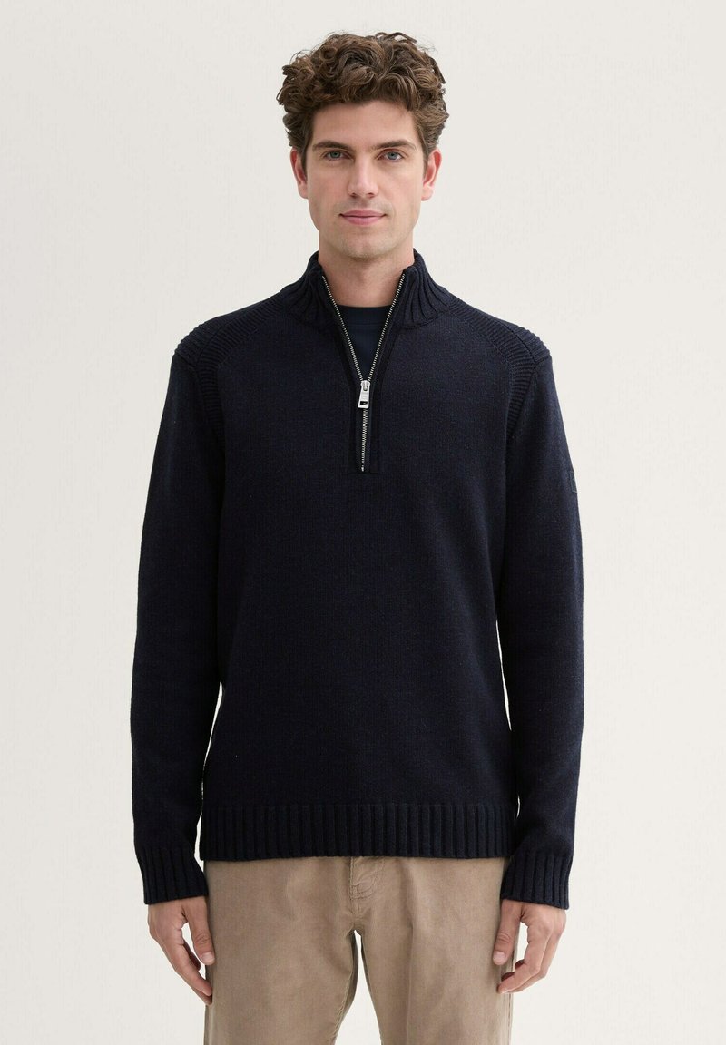 Marineblaue Strickjacke mit Reißverschluss und geripptem Kragen sowie Bündchen, ausgestattet mit einem Frontreißverschluss bis zur Mitte und strukturierten Schulterdetails. Weiche Stoffoberfläche.