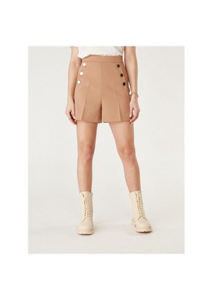 Bruna high-waisted shorts med frontveck och fem runda silverknappar; kombinerat med beige ankelstövlar och en vit topp.
