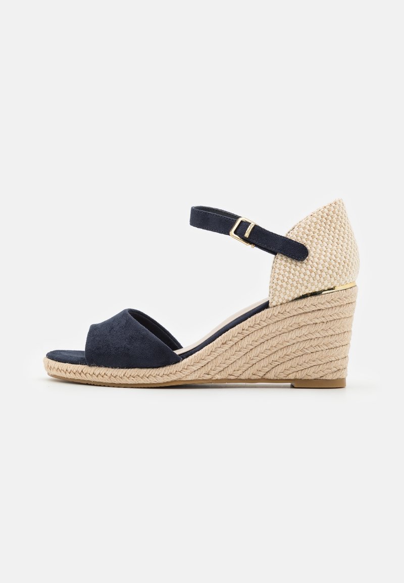 Sandale compensée bleu marine à bout ouvert avec talon beige tissé, bride de cheville ajustable avec boucle dorée et semelle plateforme en corde tressée.