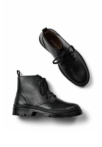 Botas de cuero negro hasta el tobillo con punteras redondas, cordones en la parte delantera, acabado texturizado, talón reforzado y suelas de goma con un profundo dibujo.