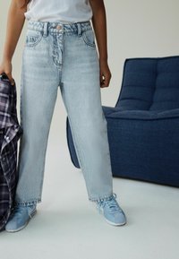 Blugi bleu cu talie înaltă și croială lejeră, cu textură estompată, buzunare frontale și nasture argintiu, asortați cu adidași bleu.