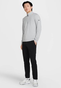 Világosszürke hosszú ujjú cipzáras ing bordázott mintával, fekete nadrággal és fehér tornacipővel párosítva. Nike logó a bal ujján.