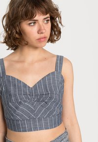 Top cropped em azul e branco com riscas, com decote em coração, alças largas e um painel frontal texturizado com um detalhe plissado.