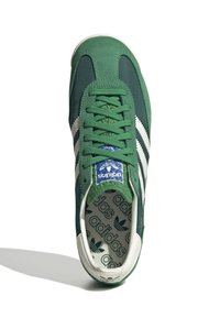 Zapatillas de ante verde y textil con rayas y acentos blancos, que presentan una etiqueta en la lengüeta azul y una plantilla estampada, punta redonda y suela blanca.