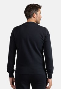 Felpa nera con colletto rotondo, maniche lunghe e polsini a costine. Tessuto morbido, forma aderente e senza motivi o decorazioni visibili.