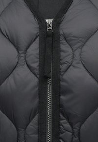 Chaqueta de plumón negra con acolchado y cuello alto, con una cremallera central y un acento texturizado en el área de la cremallera. Material suave.