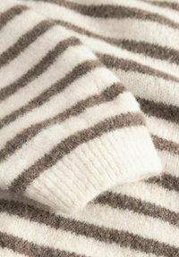 Zachte wollen stof met horizontale crème- en bruine strepen, een close-up van een opgevouwen mouwboord.