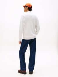 Grau gestrickter Pullover mit hohem Kragen, kombiniert mit lässigen, dunkelblauen Jeans. Accessoires bestehen aus einer orangefarbenen Mütze und schwarzen Turnschuhen.