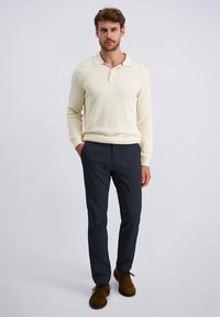 Crèmekleurige geribbelde longsleeve poloshirt met kraag, gecombineerd met donkerblauwe slim-fit broeken en een paar bruine suède schoenen.