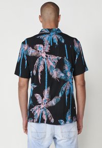 Camisa de manga corta negra con un vibrante estampado de palmeras en rosa y azul, con un corte relajado y diseño de cuello clásico.