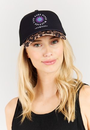 Blonde Frau trägt schwarzen Tanktop und schwarzen Truckerhut mit Leopardenmuster-Krempe und lila Sonnenlogo mit der Aufschrift "Laid Back Since Way Back"