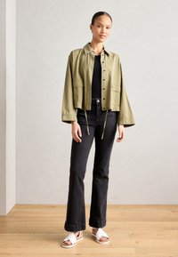 Cropped olive green jacket with button closure and two front pockets, paired with black flared jeans and white platform sandals.