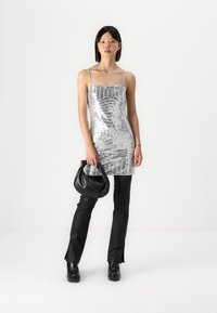 Silver sequined dress with thin straps, fitted design, and a straight cut; paired with black flared trousers and a black handbag.