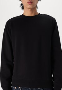 Sudadera negra en una suave mezcla de algodón, con cuello redondo y puños y dobladillo acanalados. Diseño simple sin patrones ni logotipos visibles.