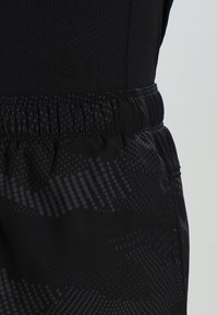 Svart sportshorts med elastiskt midjeband. Har en texturerad tyg med ett gradient prickmönster på den nedre delen.