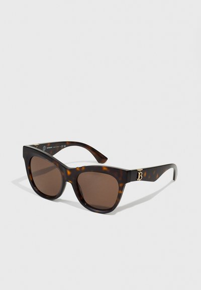 Lunettes de soleil écaille de tortue avec verres marron. Elles possèdent une large monture et un accent de logo doré sur la branche. Matériau en plastique lisse et brillant.