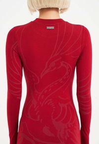 Top ajustado de manga larga rojo con un sutil estampado tonal de un diseño de pájaro en la parte posterior, con escote redondo y detalle de etiqueta en el cuello.