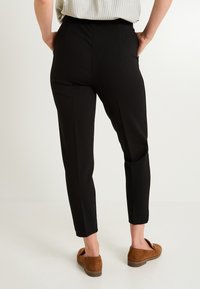 Pantalones negros ajustados con una textura suave, que cuentan con bolsillos laterales y una cinturilla alta, combinados con mocasines de ante marrón.