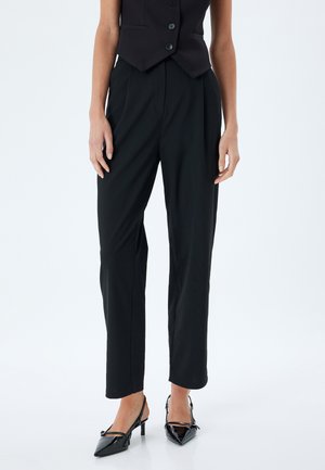 Black tailored trousers with a straight fit and pleats, made from a smooth fabric. Paired with black patent slingback heels.
