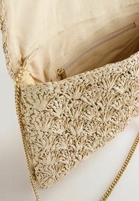Geflochtene Strohtasche in blassem Beige mit einem strukturierten Blumenmuster. Goldene Kettenriemen und ein Innenfach mit Reißverschluss und einem Stofffutter.