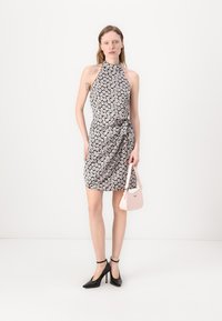 Halter neck dress with a black and white floral pattern, knotted at the waist. Paired with a small pink bag and black high heels.